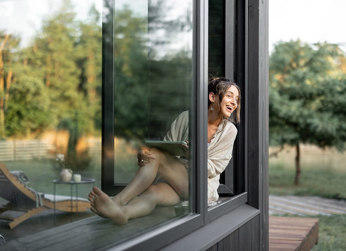 Read Our Reviews - View of a Young Woman Holding a Tablet Having Fun Sitting Next to an Open Window in her Vacation Home Enjoying the Country Views