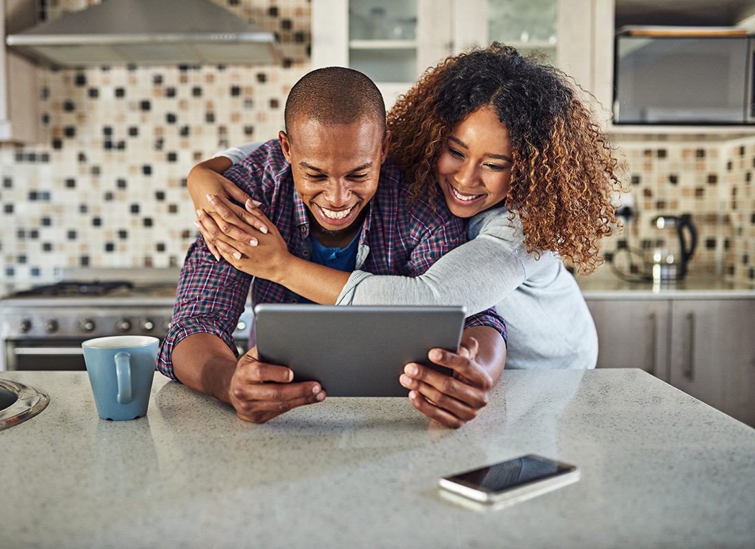 Service Center - Portrait of a Cheerful Loving Young Married Couple Spending Time Together in the Kitchen While Looking at a Tablet
